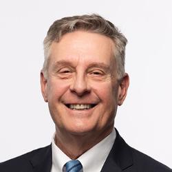 Dr. Pike has short gray hair, is wearing a dark suit with satin blue tie, and is smiling at the camera.