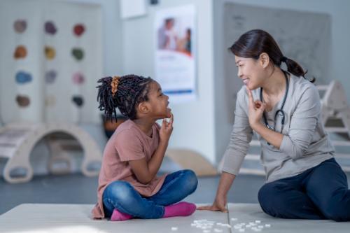 Therapist and girl sitting crosslegged touching chins