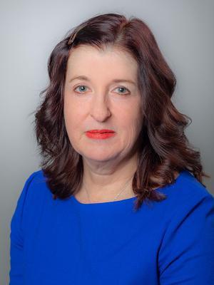 Dr. Hanrahan has long wavy reddish-brown hair, is wearing a blue blouse, and is smiling at the camera