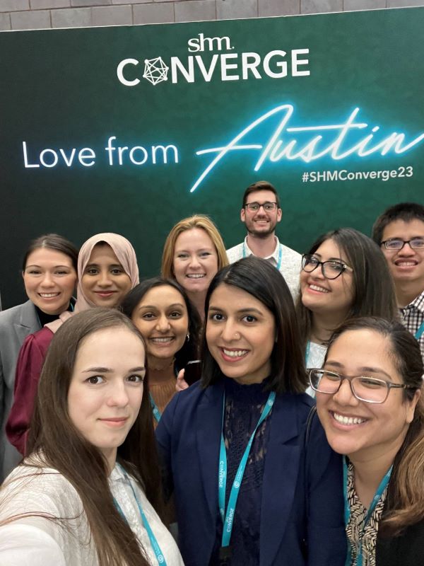 A group of people smiling in front of a decorative poster at the Society of Hospital Medicine conference.